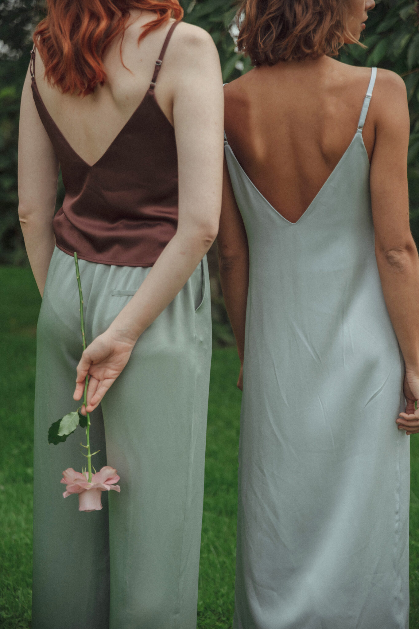two girls from the back in silk clothing, one holding a flower